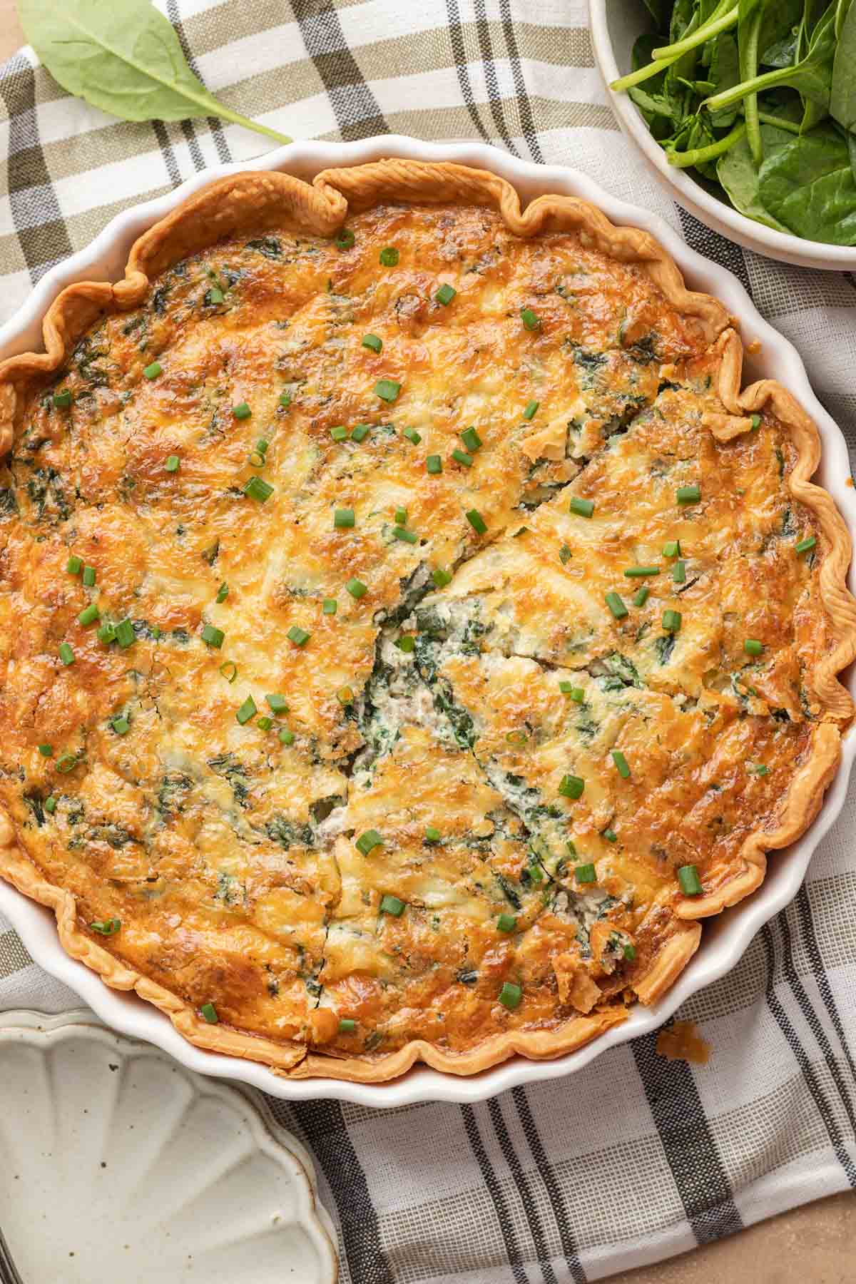 Golden-brown spinach sausage quiche in a pie dish, partially sliced, with green herbs sprinkled on top.