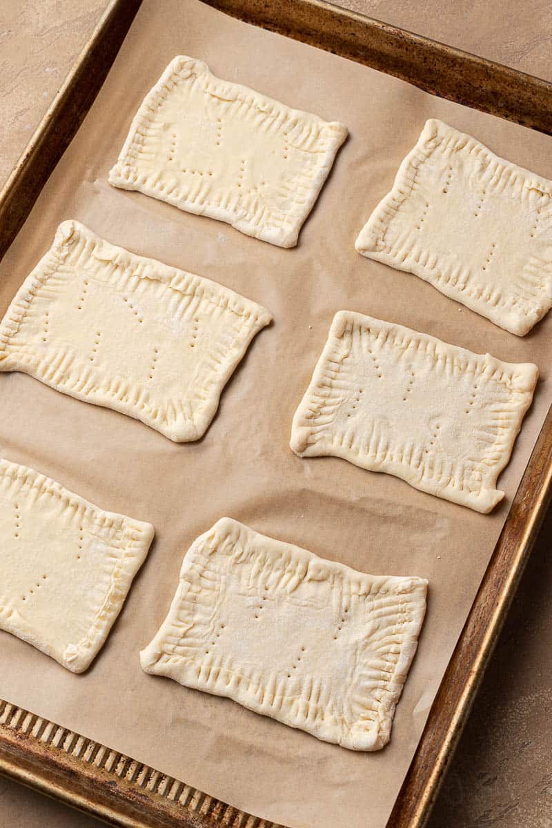 Six unbaked rectangular pastries with crimped edges on parchment paper on a baking sheet.