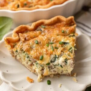 A slice of spinach & sausage quiche with cheese, garnished with chopped chives on a white plate.