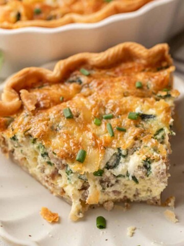 A slice of spinach & sausage quiche with cheese, garnished with chopped chives on a white plate.