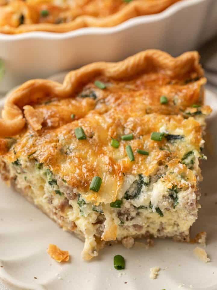 A slice of spinach & sausage quiche with cheese, garnished with chopped chives on a white plate.