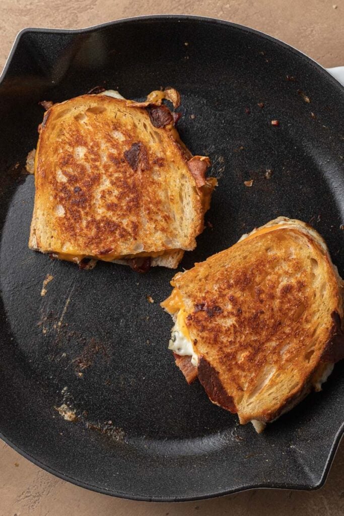 Two grilled cheese sandwiches cooking in a black skillet with golden, crispy bread.