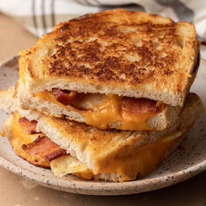 Grilled cheese sandwich with bacon, cut in half and stacked on a speckled ceramic plate.