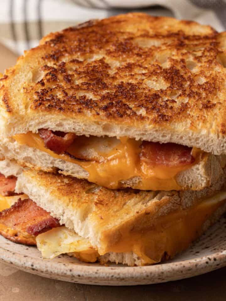 Grilled cheese sandwich with bacon, cut in half and stacked on a speckled ceramic plate.