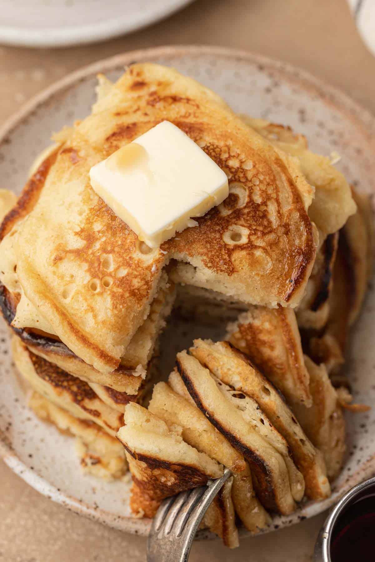 A stack of pancakes topped with butter, with a wedge cut out and a fork holding the slice.