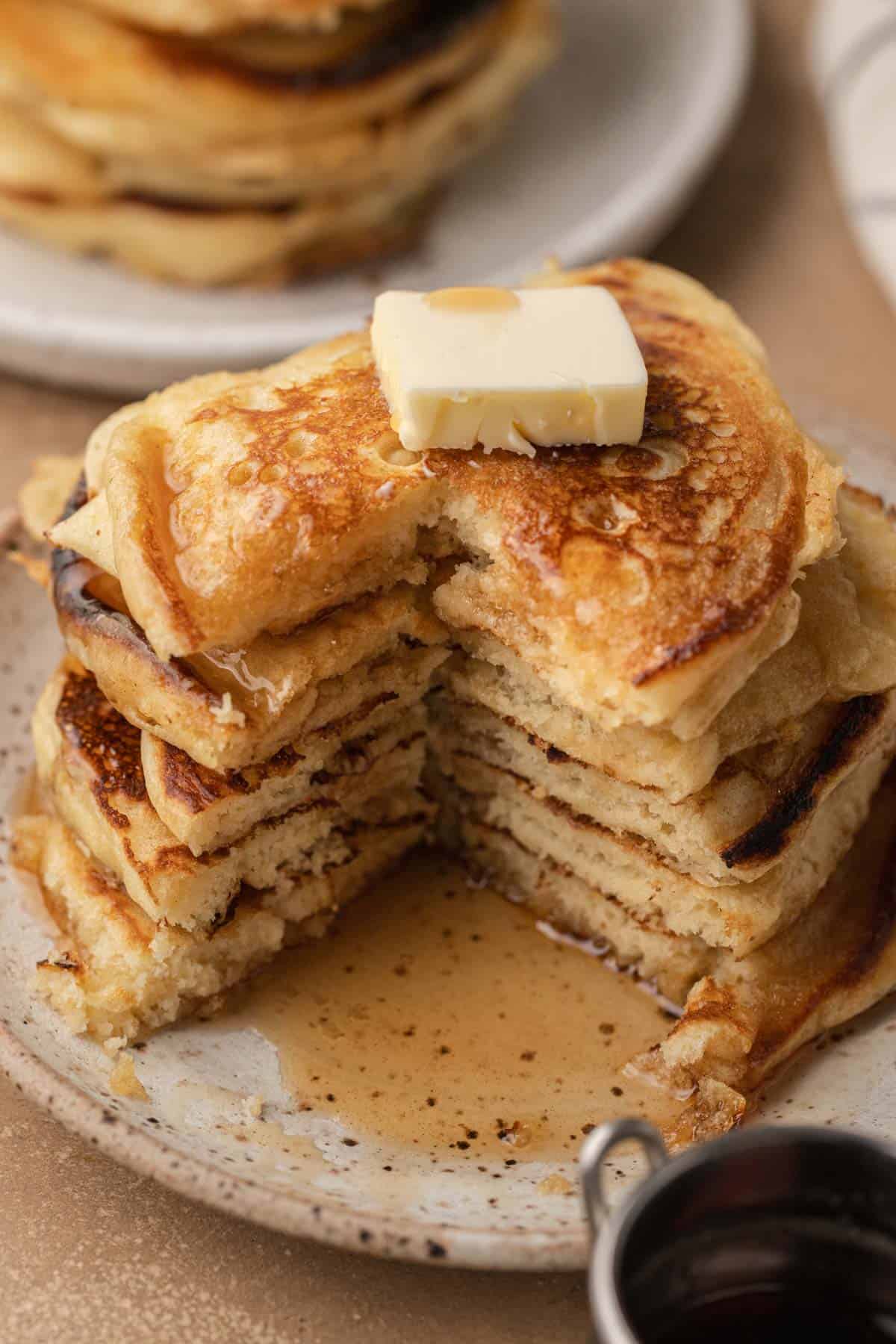 A stack of pancakes with a pat of butter and syrup, with a triangular section cut out on a ceramic plate.