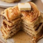 A stack of fluffy pancakes with a pat of butter and syrup, showing a wedge cut out on a plate.