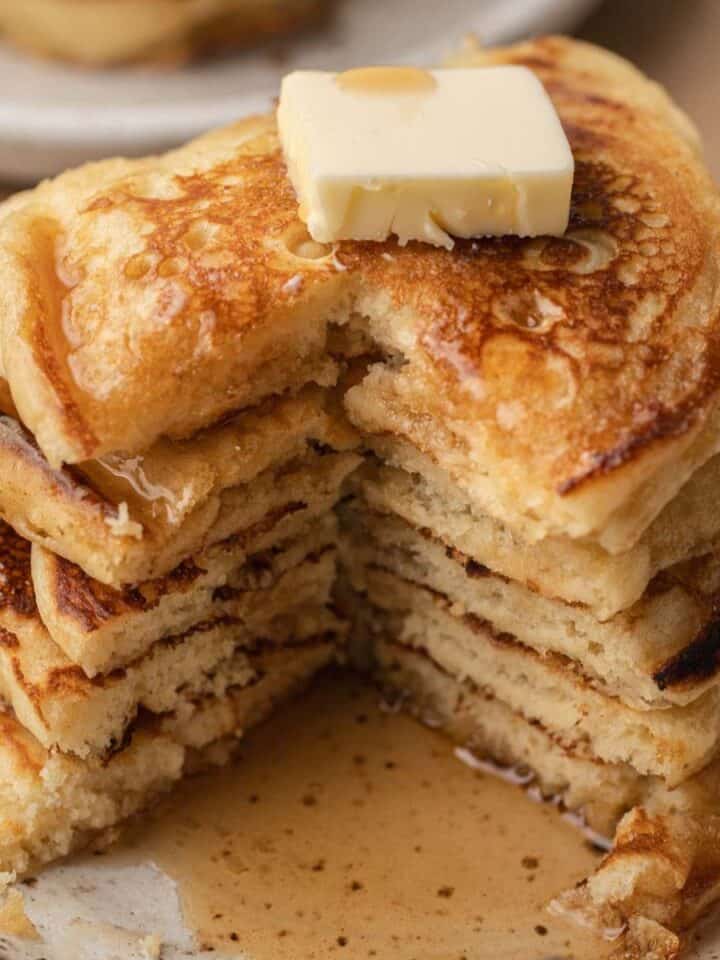 A stack of fluffy pancakes with a pat of butter and syrup, showing a wedge cut out on a plate.