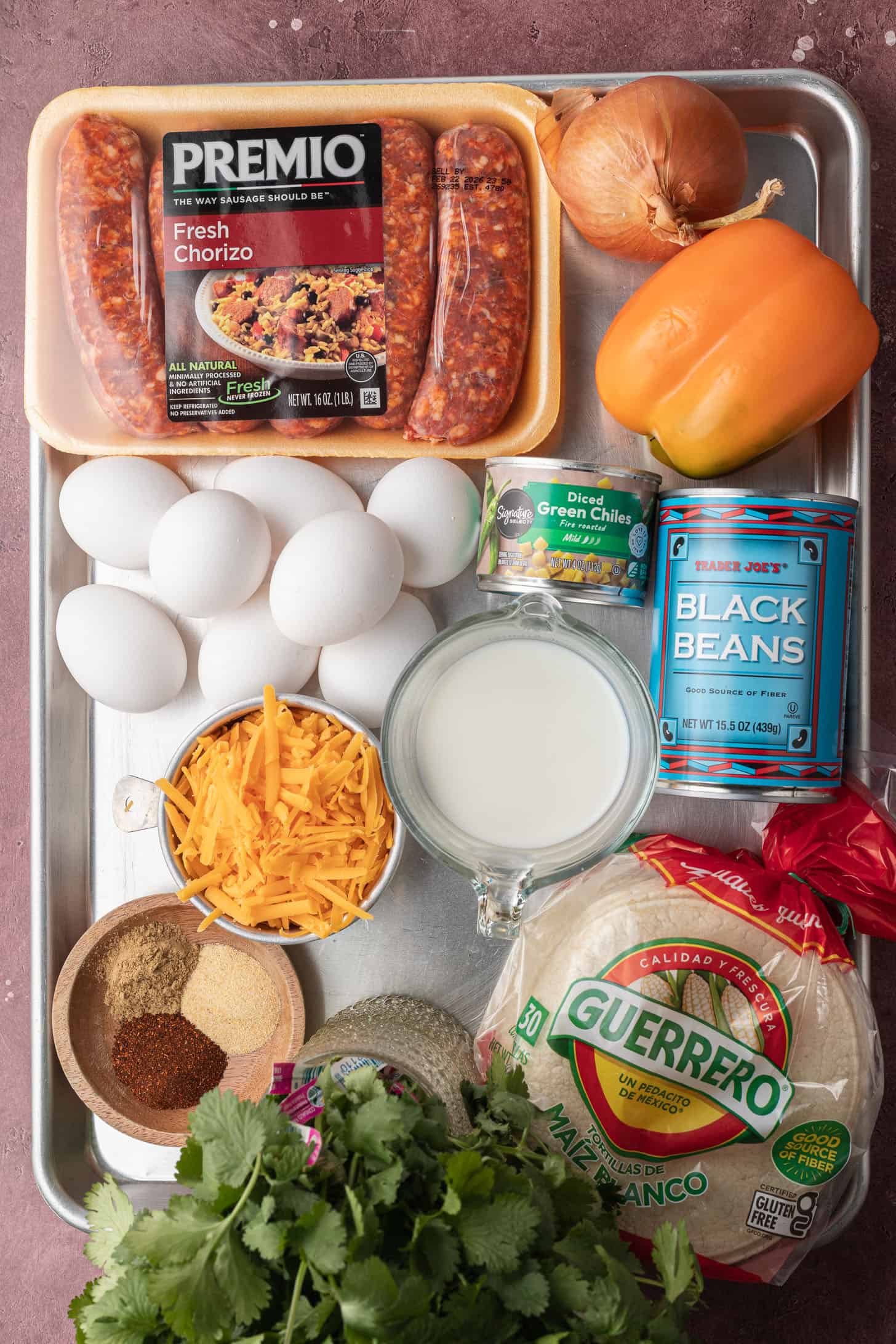 Breakfast casserole ingredients: chorizo, eggs, cheddar, milk, black beans, green chiles, onion, pepper, tortillas, spices.