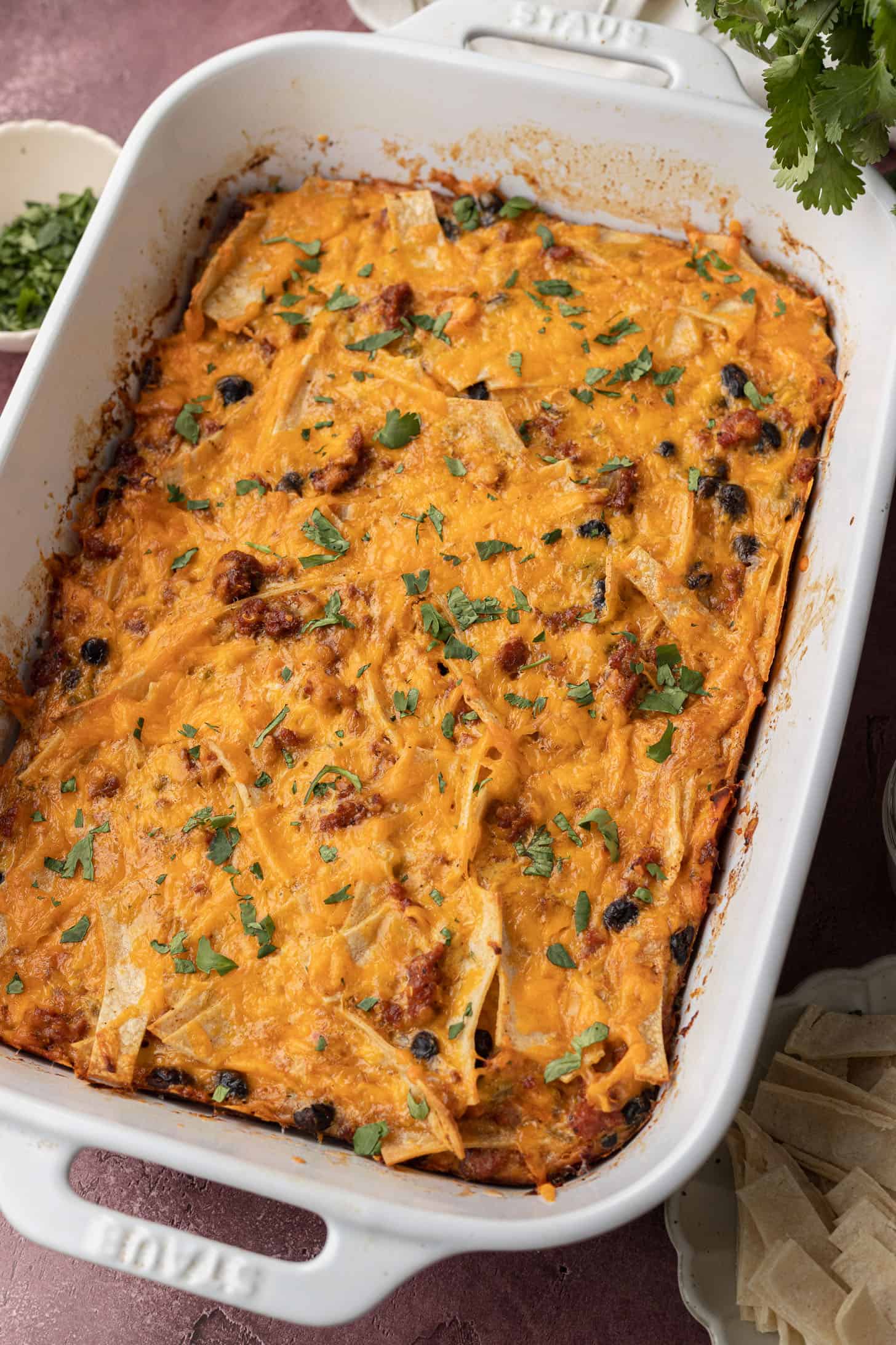 A baked casserole topped with melted cheese and cilantro in a white dish, with crispy edges and visible beans.