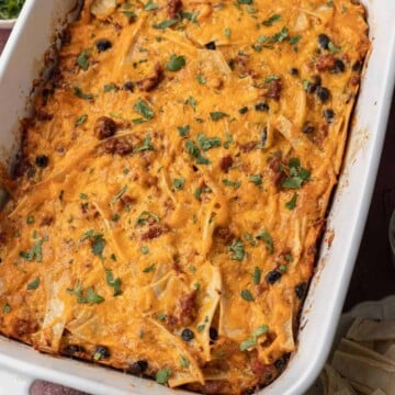 Baked cheesy casserole with tortilla strips, black beans, and herbs in a white dish.
