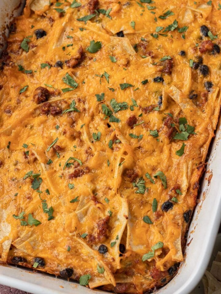 Baked cheesy casserole with tortilla strips, black beans, and herbs in a white dish.