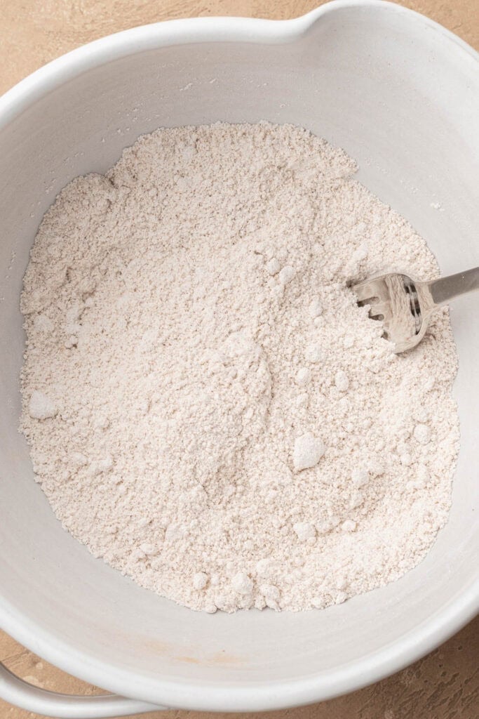A white mixing bowl with flour mixture and a metal fork inside.