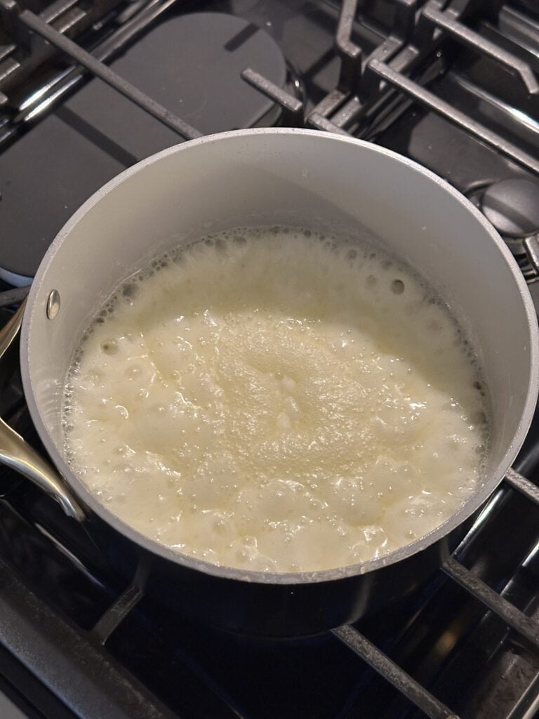 A pot of liquid boiling on a gas stove burner, creating bubbles and steam.