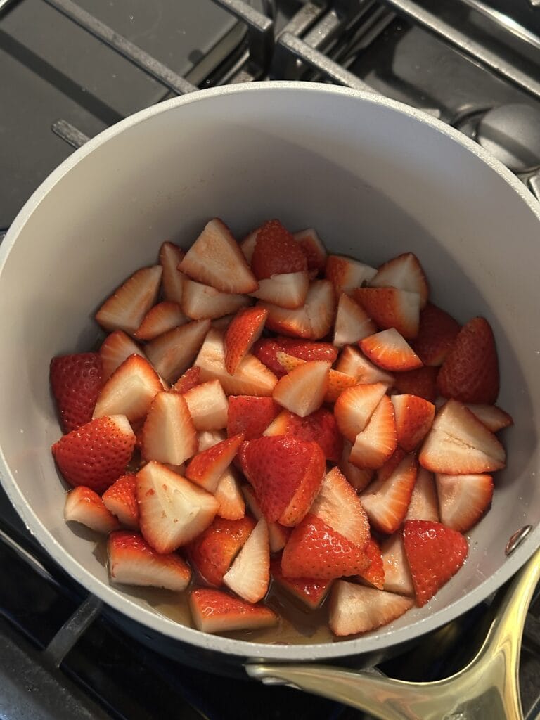 Sliced strawberries in a white pot on a stove, ready to be cooked.