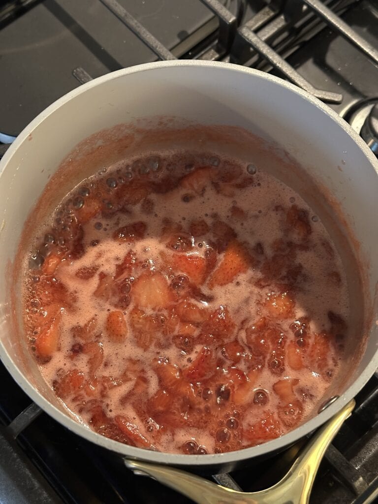 Strawberries simmering in a pot on a stovetop, creating a bubbling, foamy mixture.