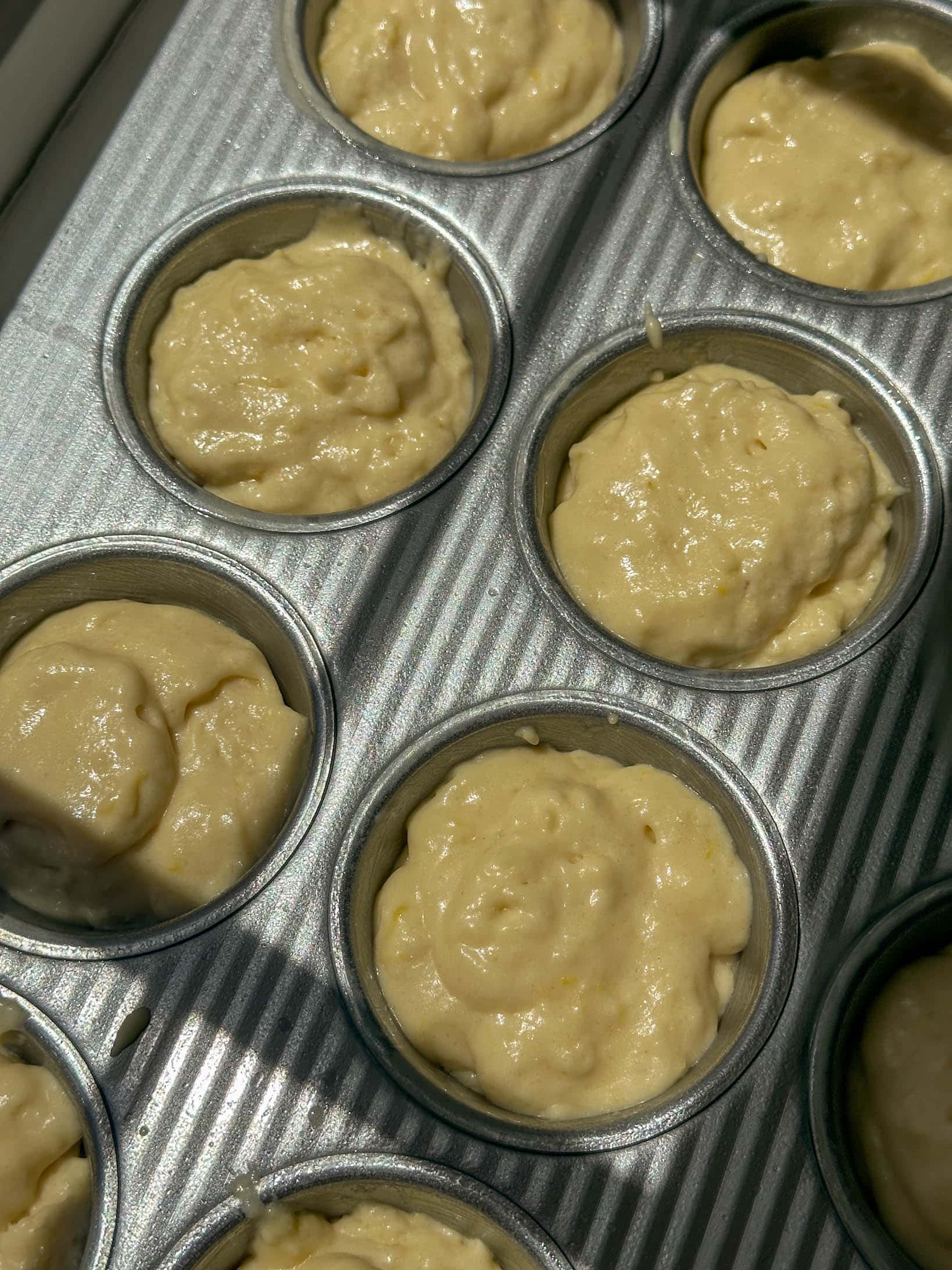 Close-up of raw lemon muffin batter in a metal muffin tin, ready to be baked.