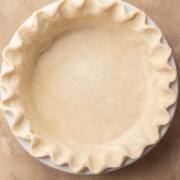 Unbaked pie crust with crimped edges in a white pie dish on a tan surface.