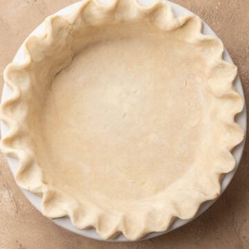 Unbaked pie crust with crimped edges in a white pie dish on a tan surface.
