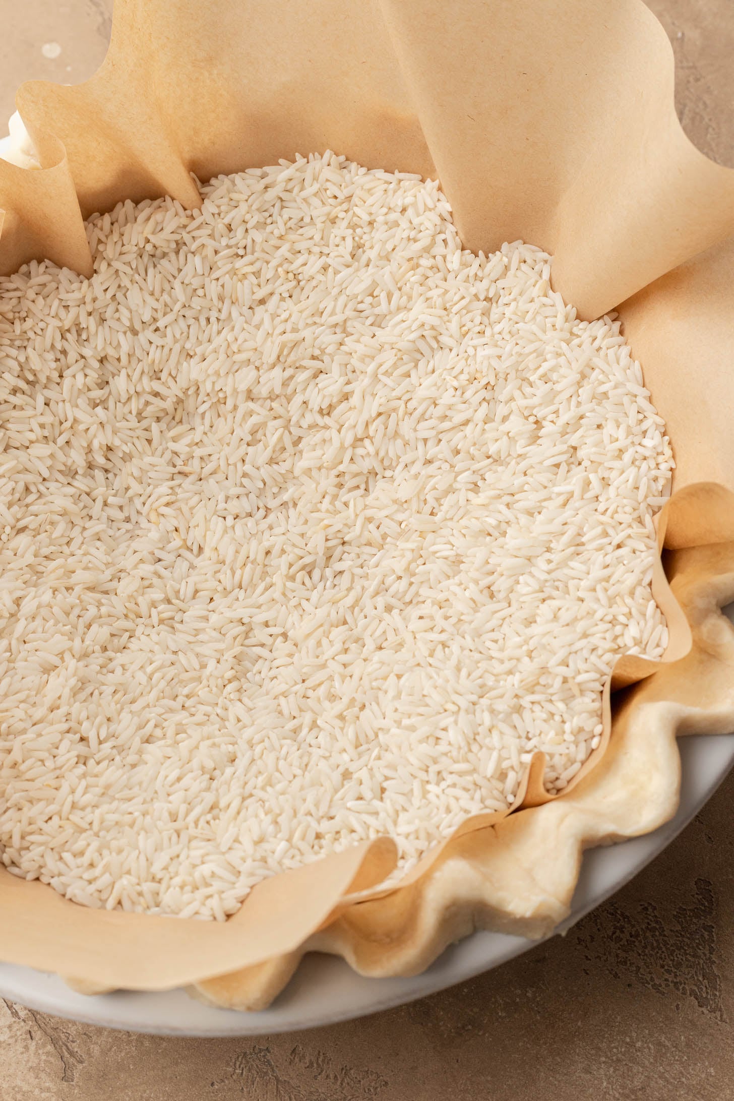 Unbaked quiche pie crust lined with parchment paper and filled with uncooked rice for blind baking.