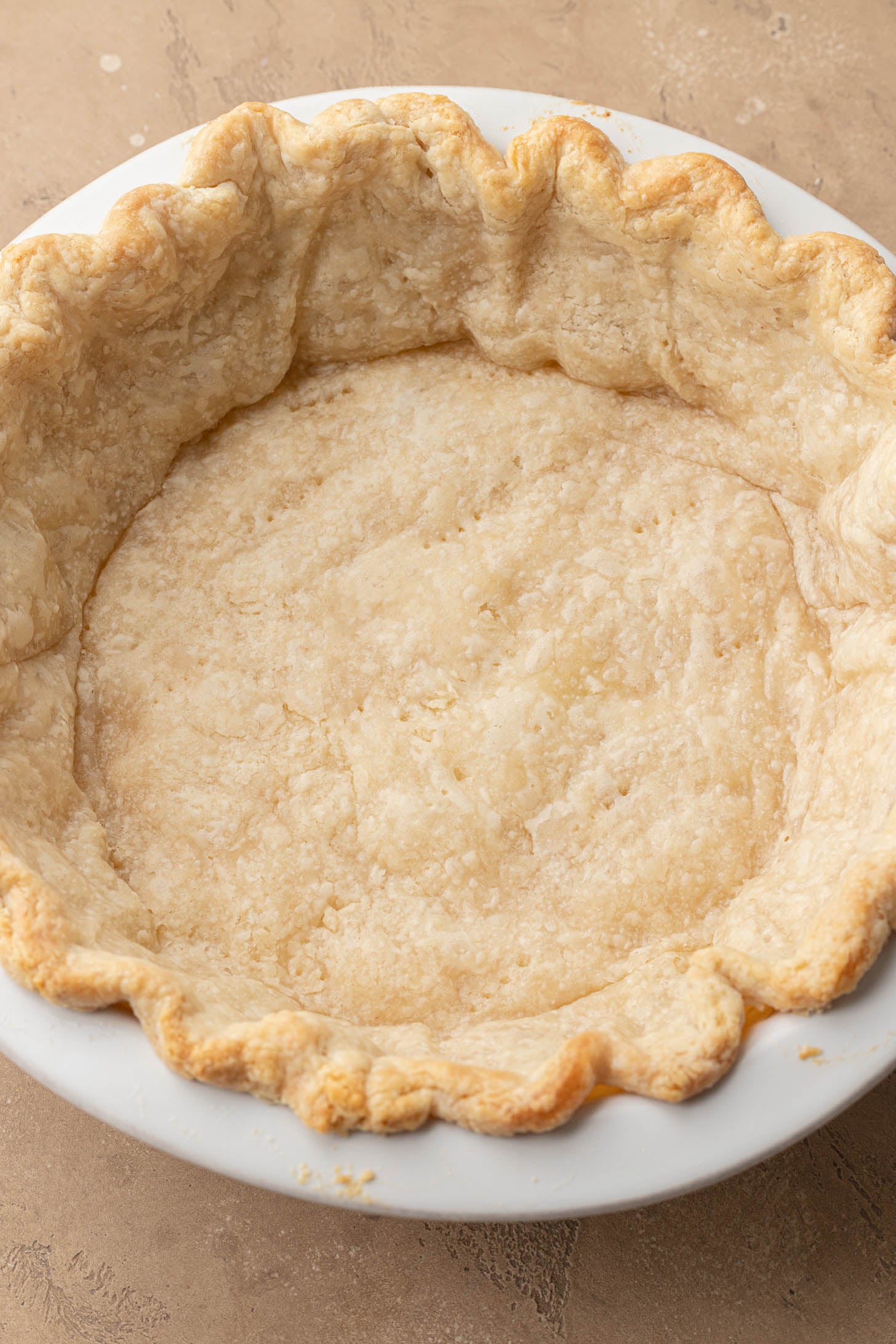 A baked, empty quiche pie crust in a white pie dish rests on a tan surface.