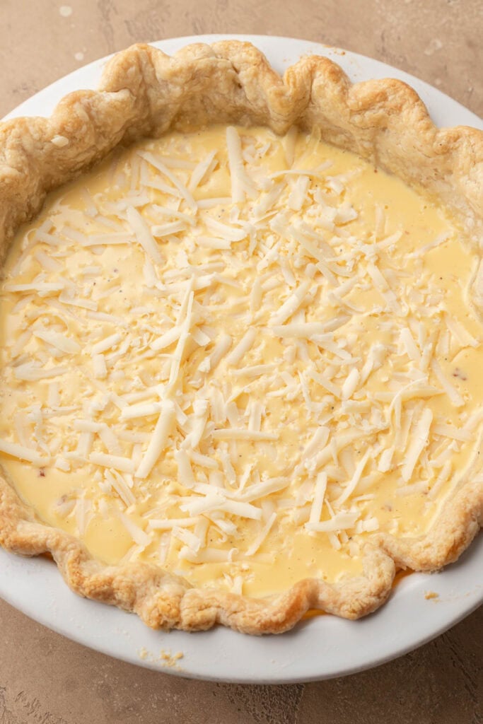 Unbaked quiche in a pie crust, filled with egg mixture and topped with shredded cheese.
