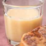 A glass of creamy syrup next to slices of bread on a plate.