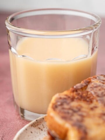 A glass of creamy syrup next to slices of bread on a plate.
