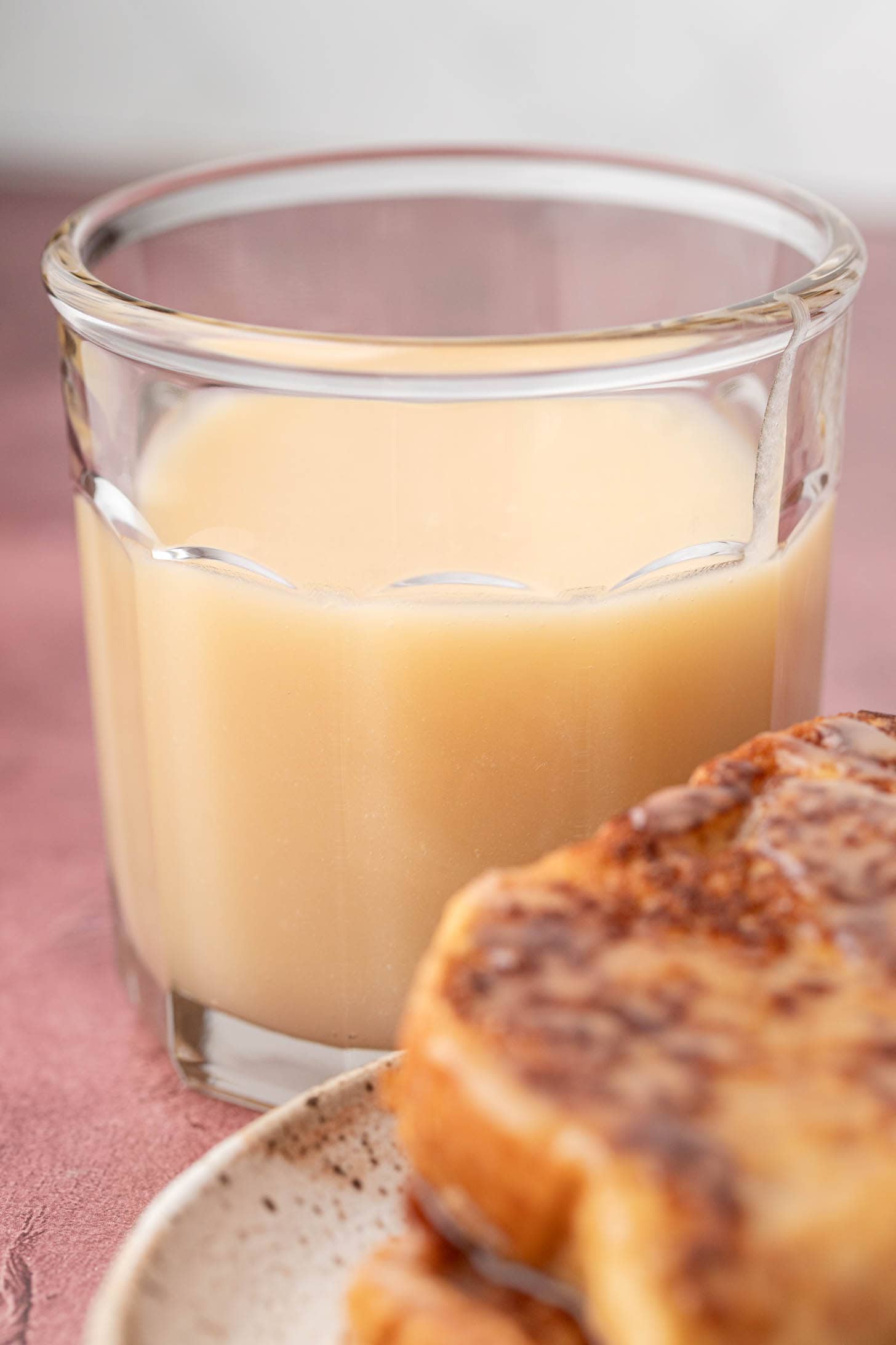 A glass of creamy syrup next to slices of bread on a plate.