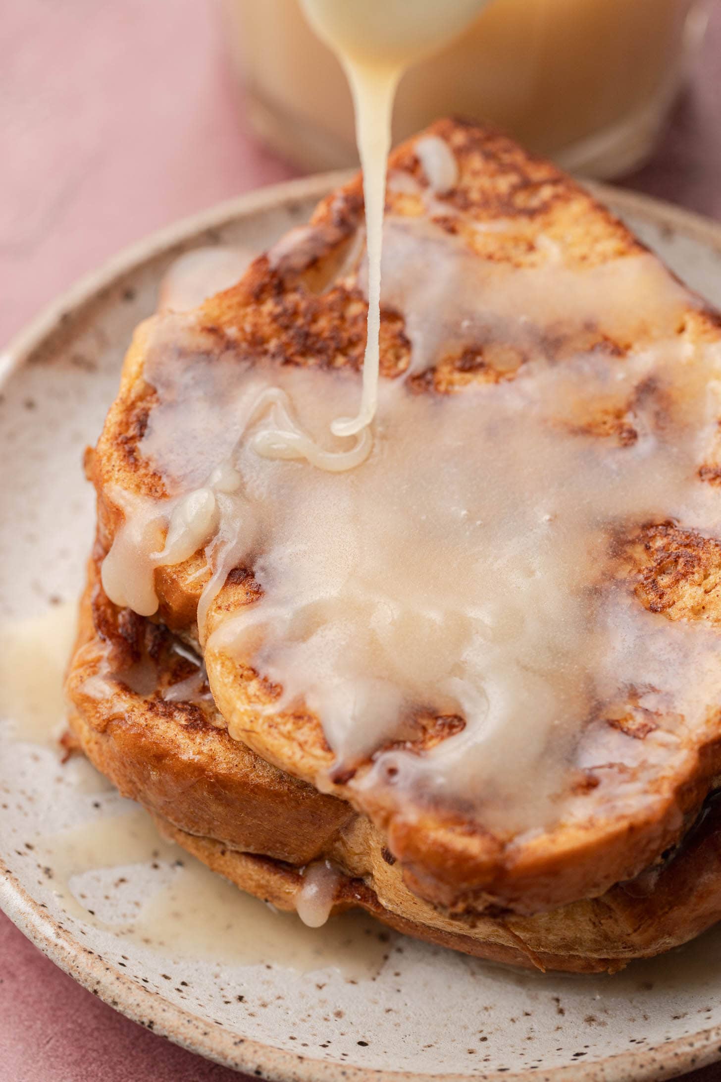 Two slices of French toast on a plate being drizzled with a creamy buttermilk sauce.