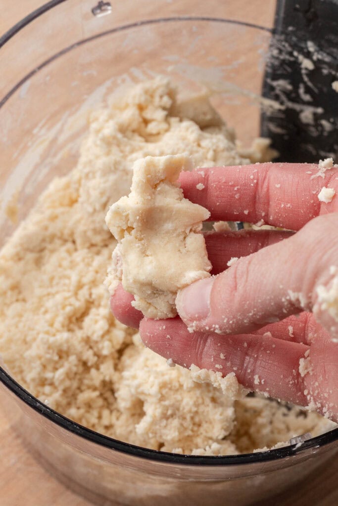 A hand holds a clump of crumbly dough over a bowl of more dough mixture.