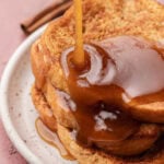 Syrup being poured over stacked slices of French toast on a white plate.