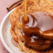 Syrup being poured over stacked slices of French toast on a white plate.