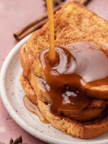 Syrup being poured over stacked slices of French toast on a white plate.