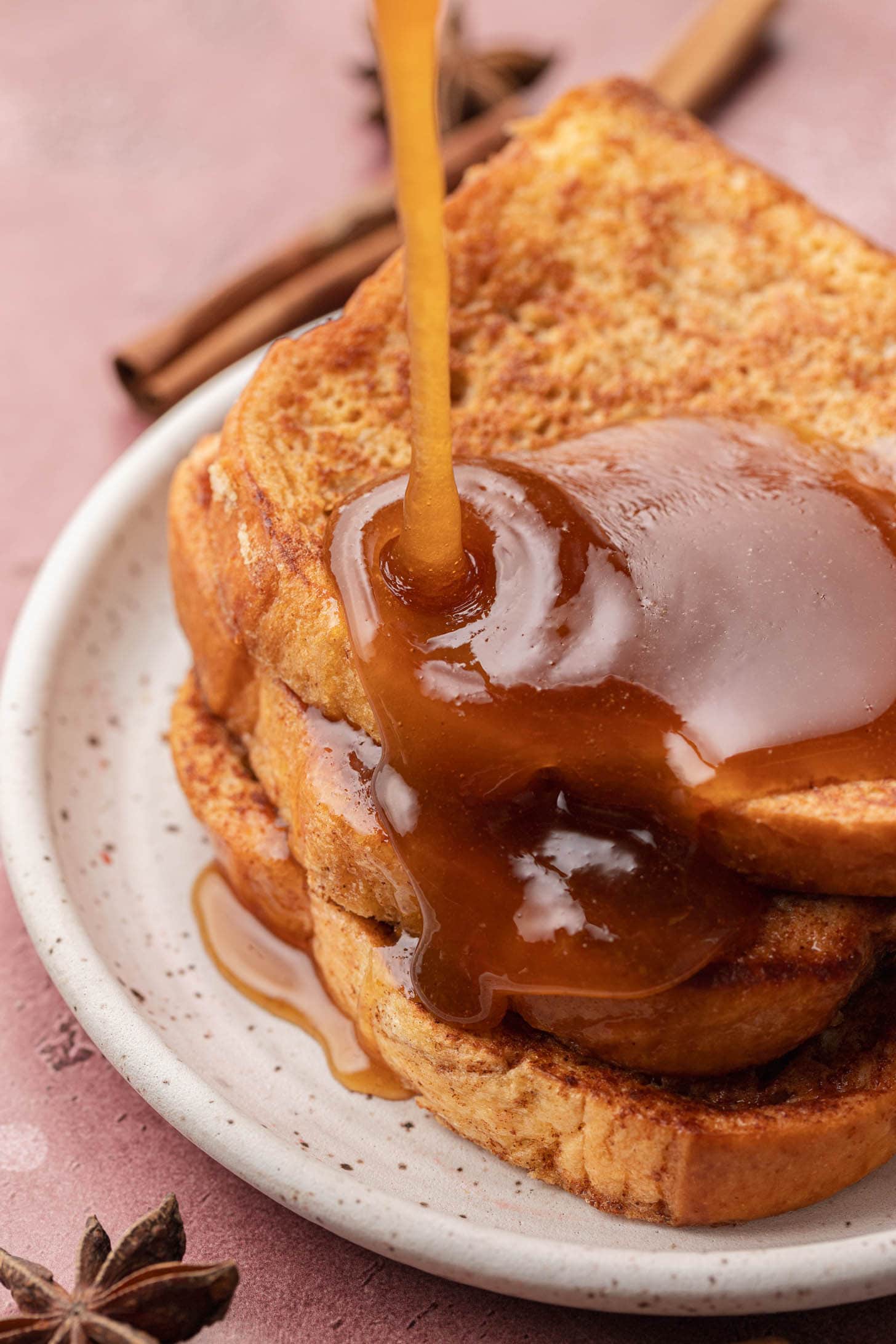 Syrup being poured over stacked slices of French toast on a white plate.