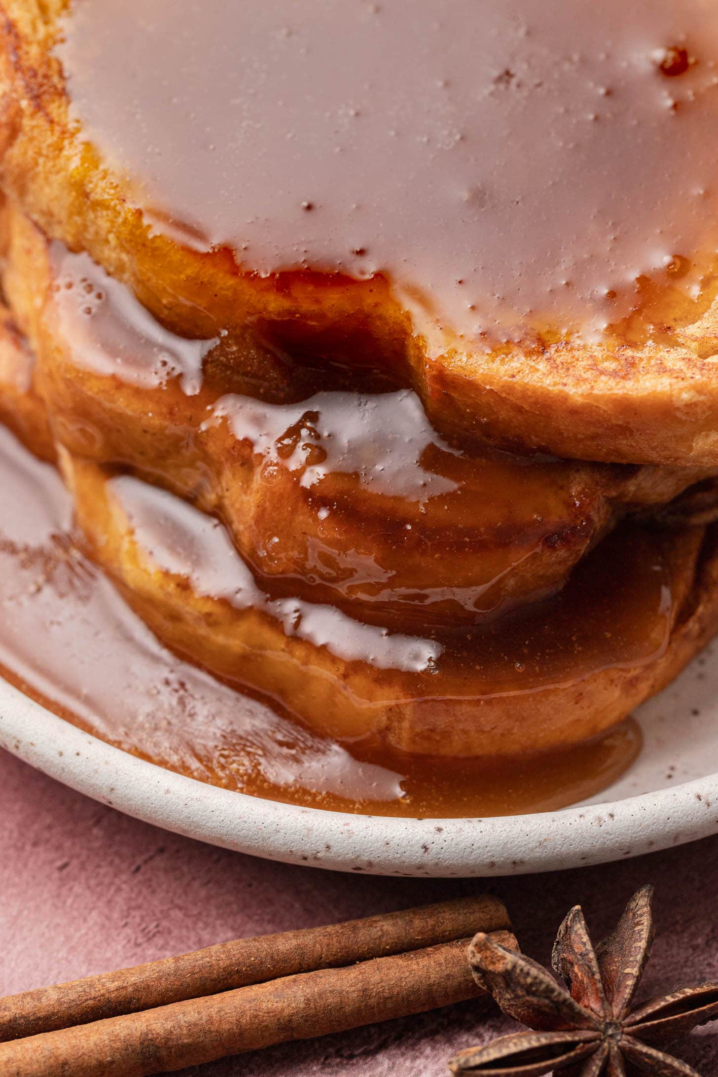 Close-up of thick French toast slices with syrup, on a plate, with cinnamon sticks and a star anise nearby.