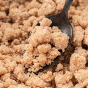 A spoon scooping crumbly brown sugar and flour streusel topping from a bowl.