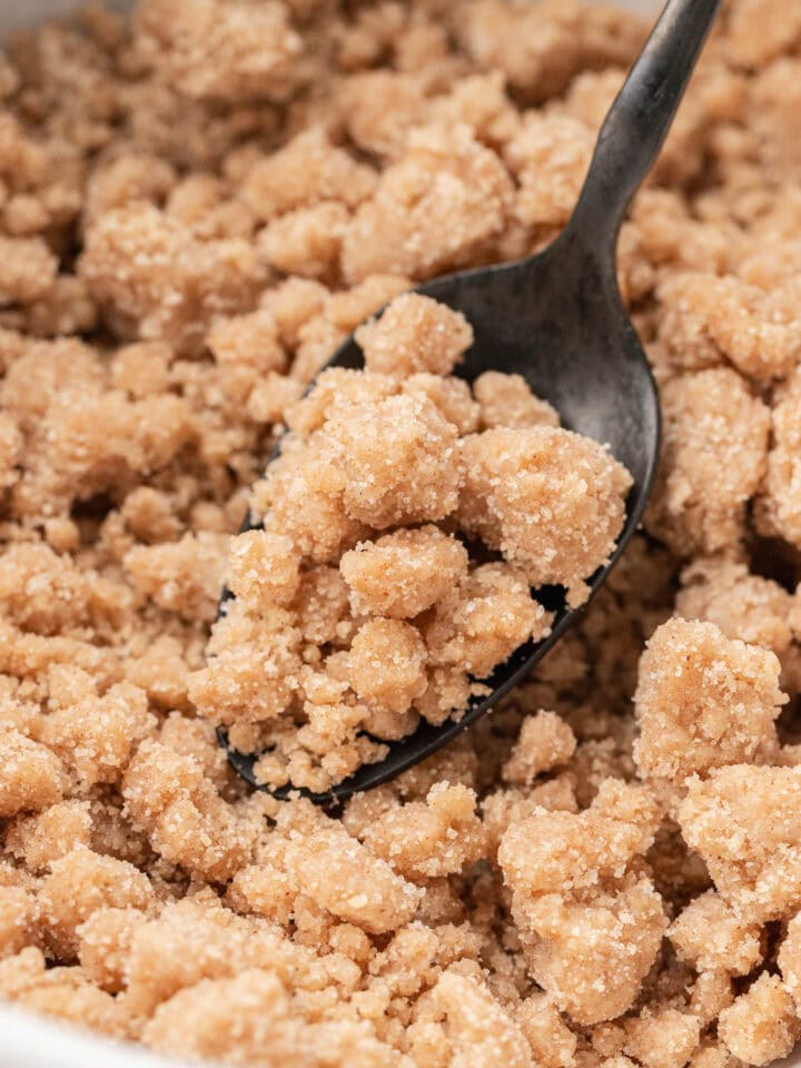 A spoon scooping crumbly brown sugar and flour streusel topping from a bowl.