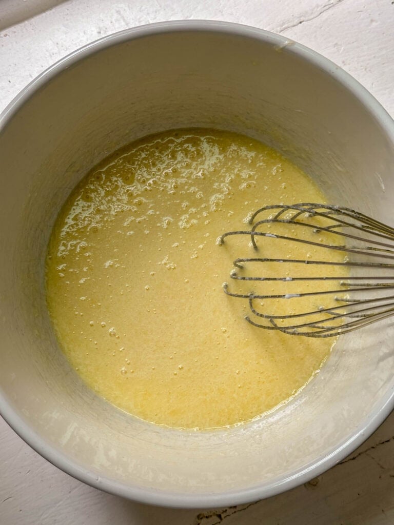 A mixing bowl with yellow batter and a metal whisk resting inside.