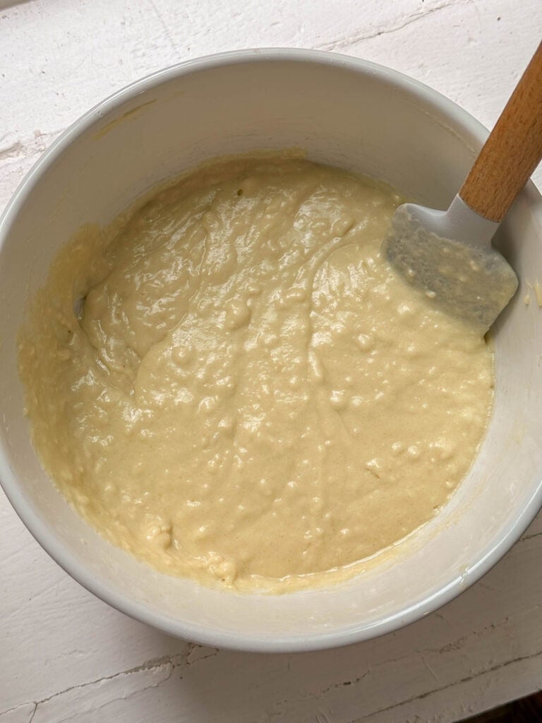 Bowl of thick, creamy batter with a spatula on a white surface.