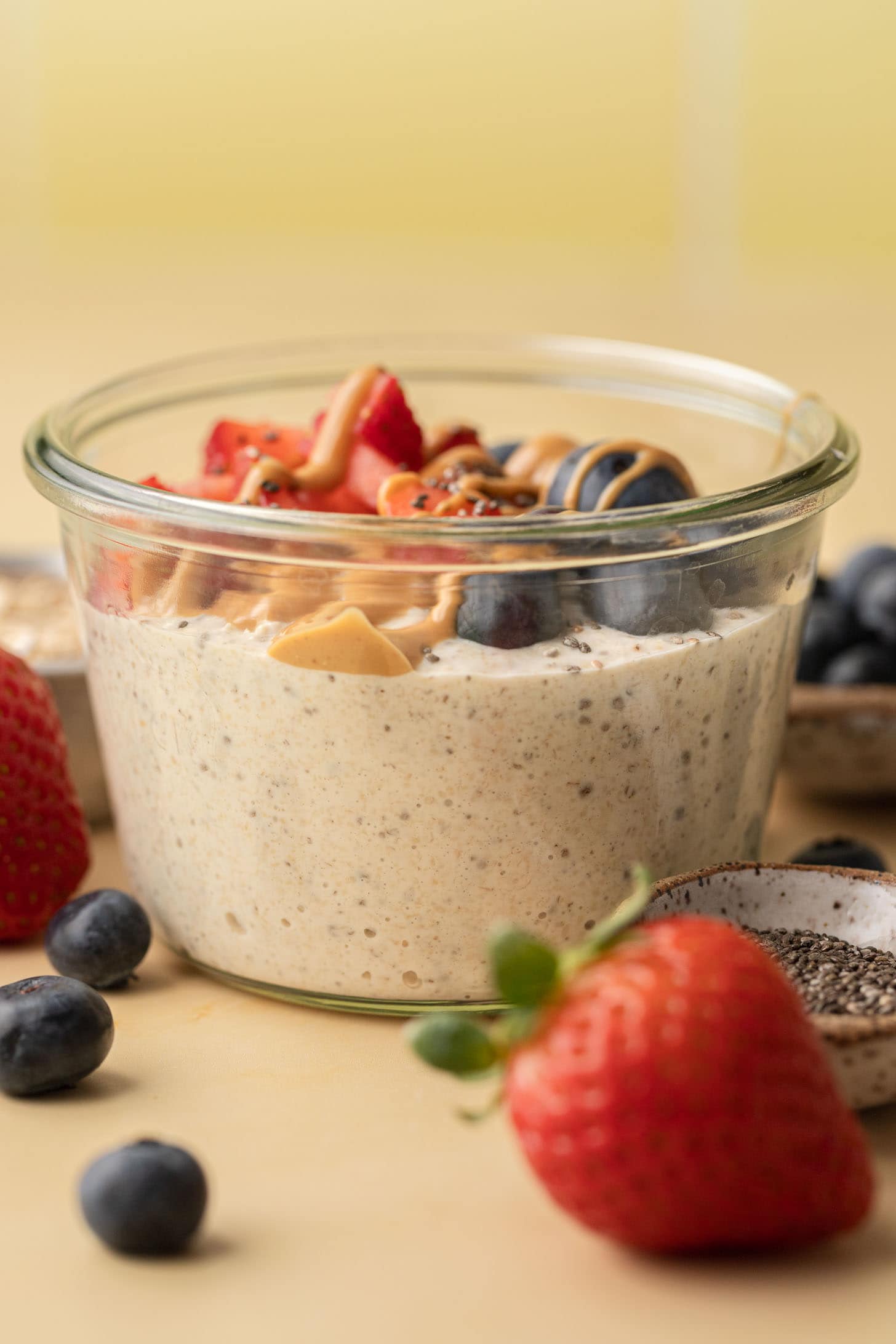 A glass jar of overnight oats topped with strawberries, blueberries, peanut butter, and chia seeds.