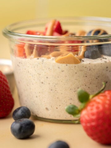 Glass jar of overnight oats topped with peanut butter, strawberries, and blueberries, with berries in front.