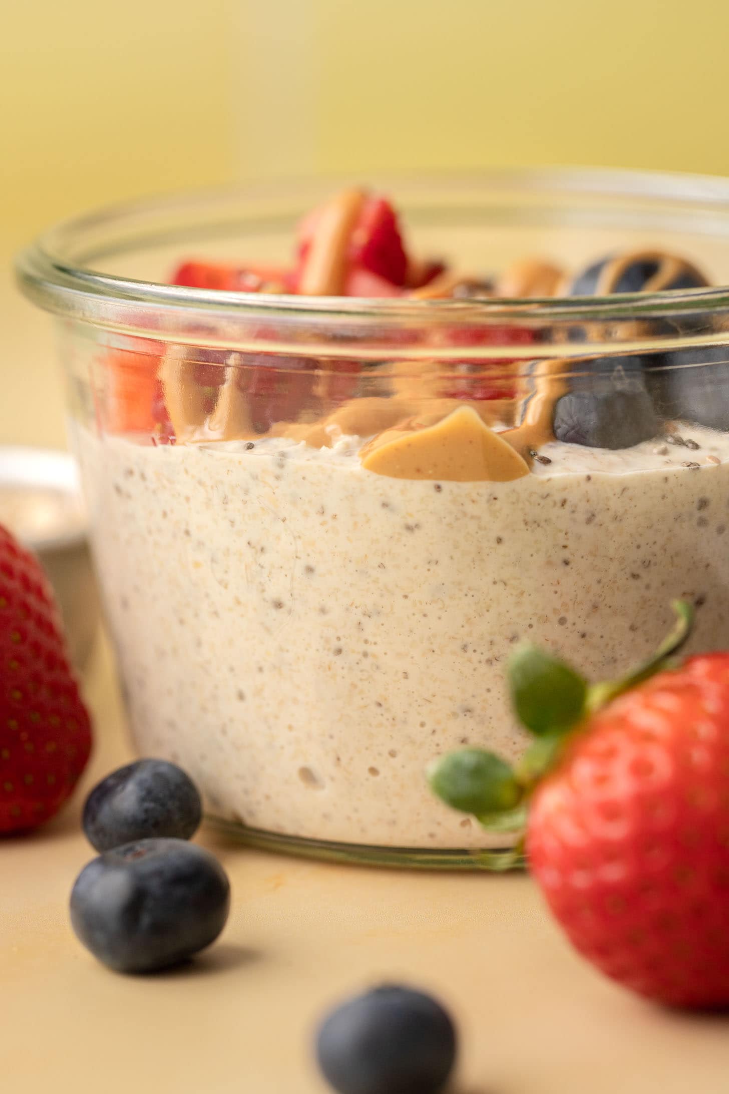 Glass jar of overnight oats topped with peanut butter, strawberries, and blueberries, with berries in front.