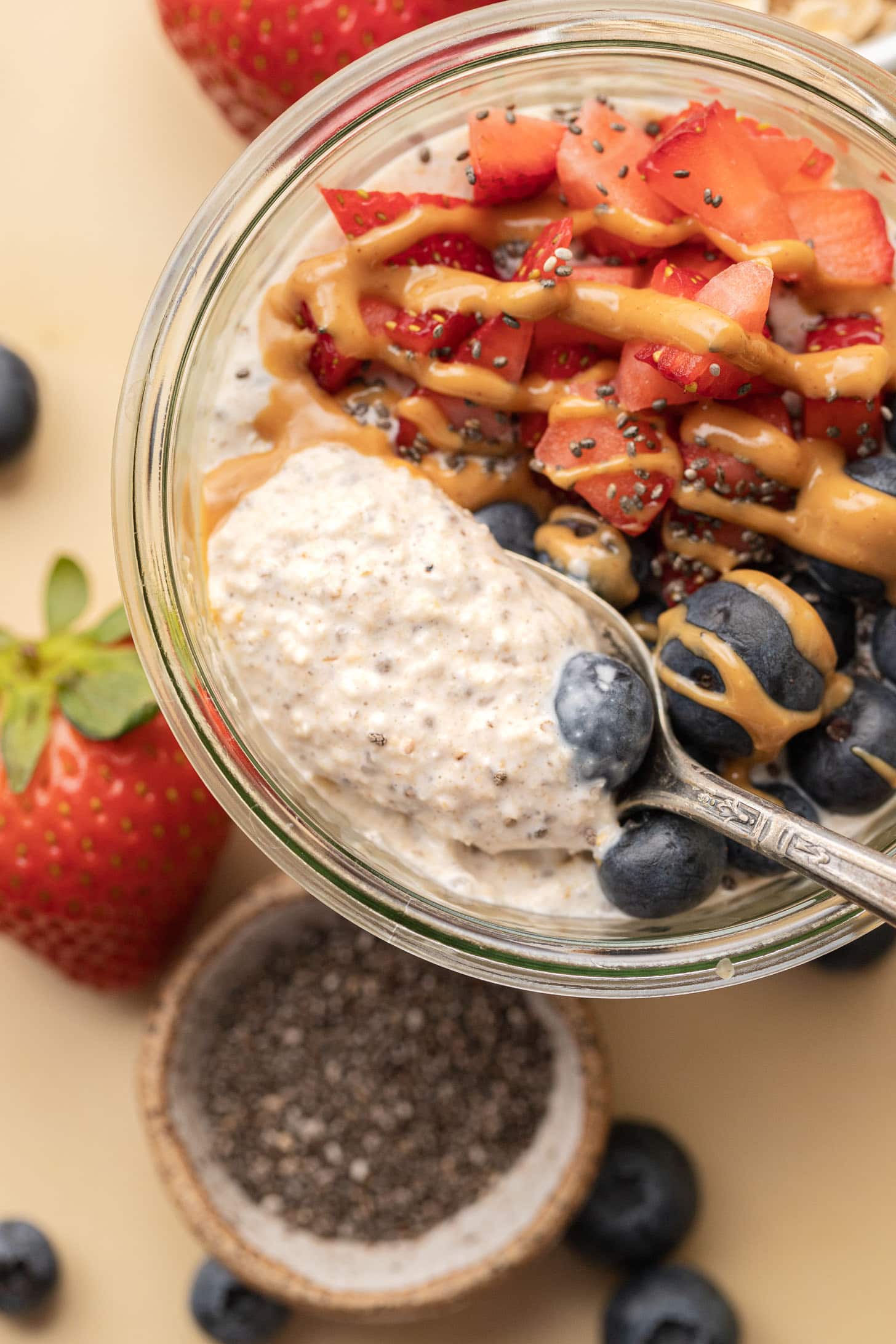 A bowl of blended overnight oats pudding topped with strawberries, blueberries, peanut butter drizzle, and chia seeds.