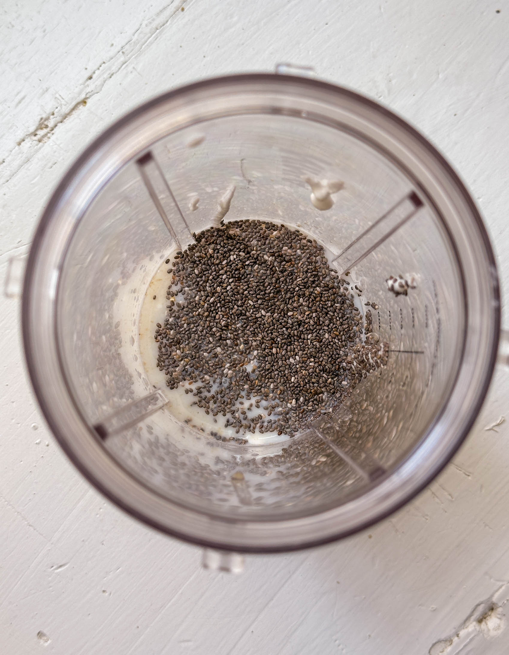 Chia seeds and liquid in a blender cup, viewed from above on a white surface.