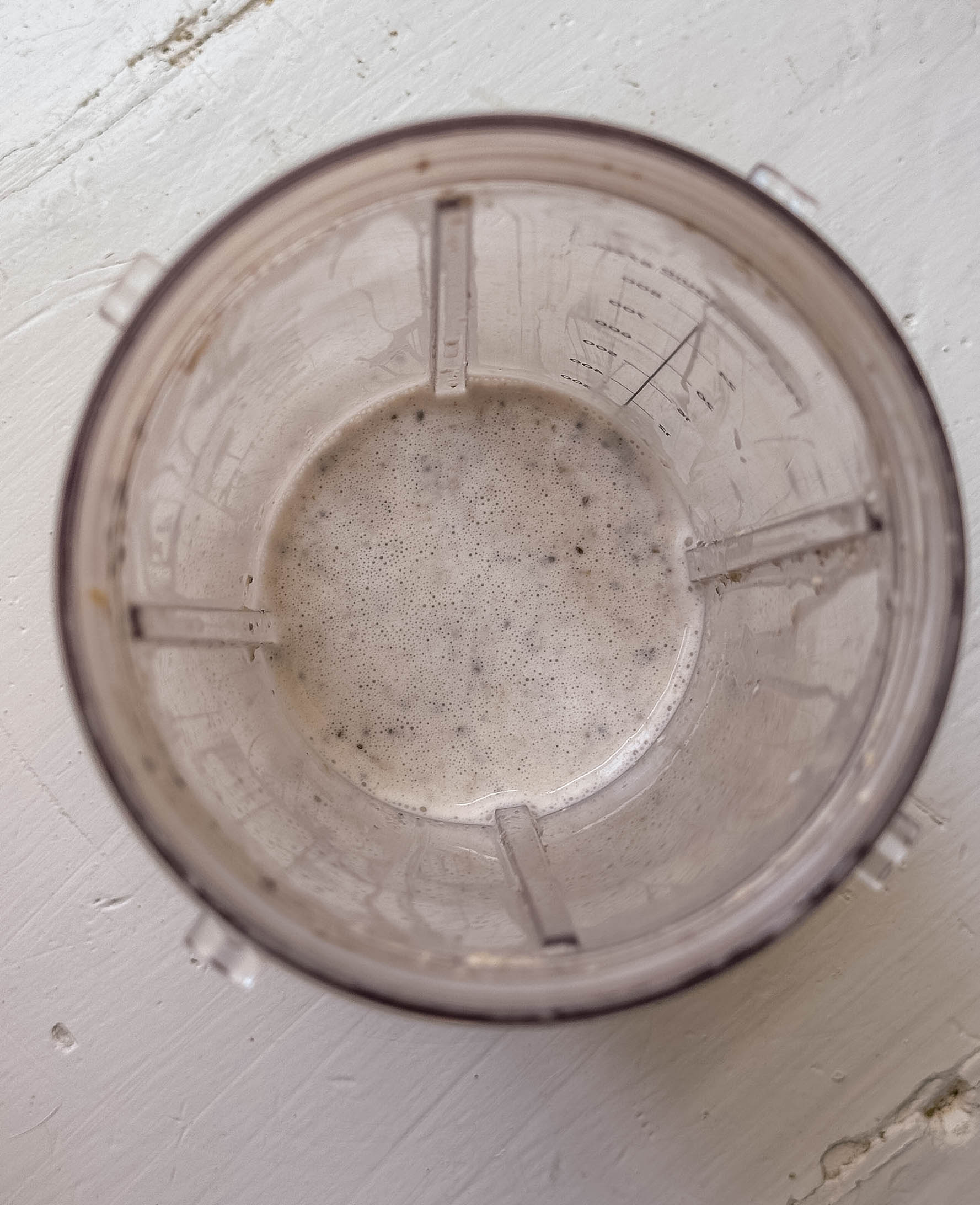 Top view of a blender cup with a small amount of frothy overnight oats at the bottom on a white surface.