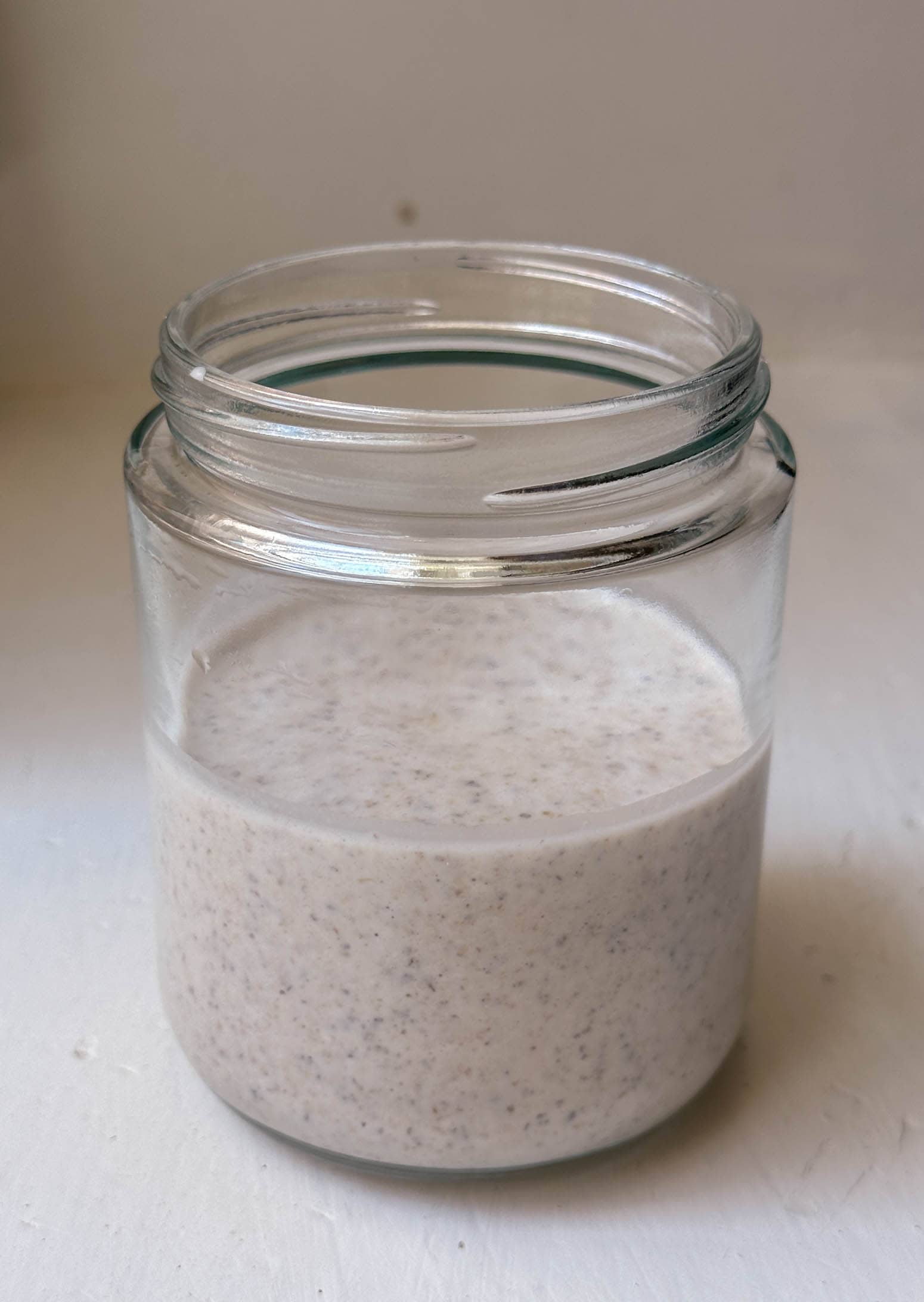 An open glass jar filled halfway with a creamy blended oat mixture sits on a white surface.