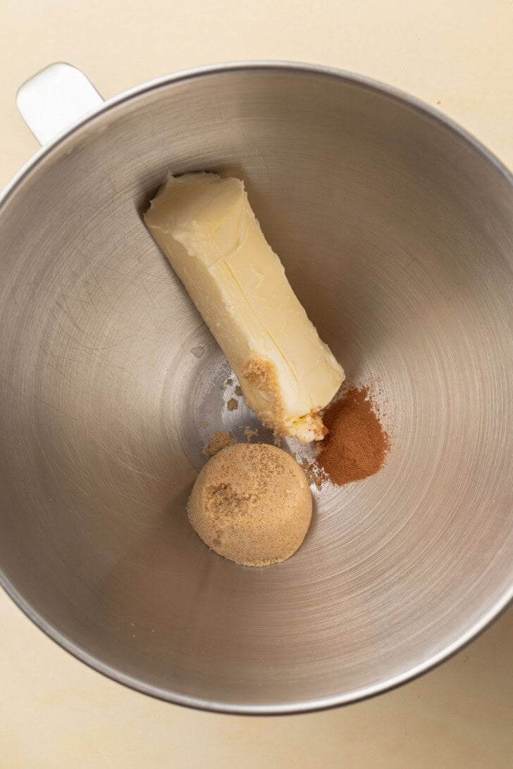A stick of butter, brown sugar, and cinnamon in a metal mixing bowl.