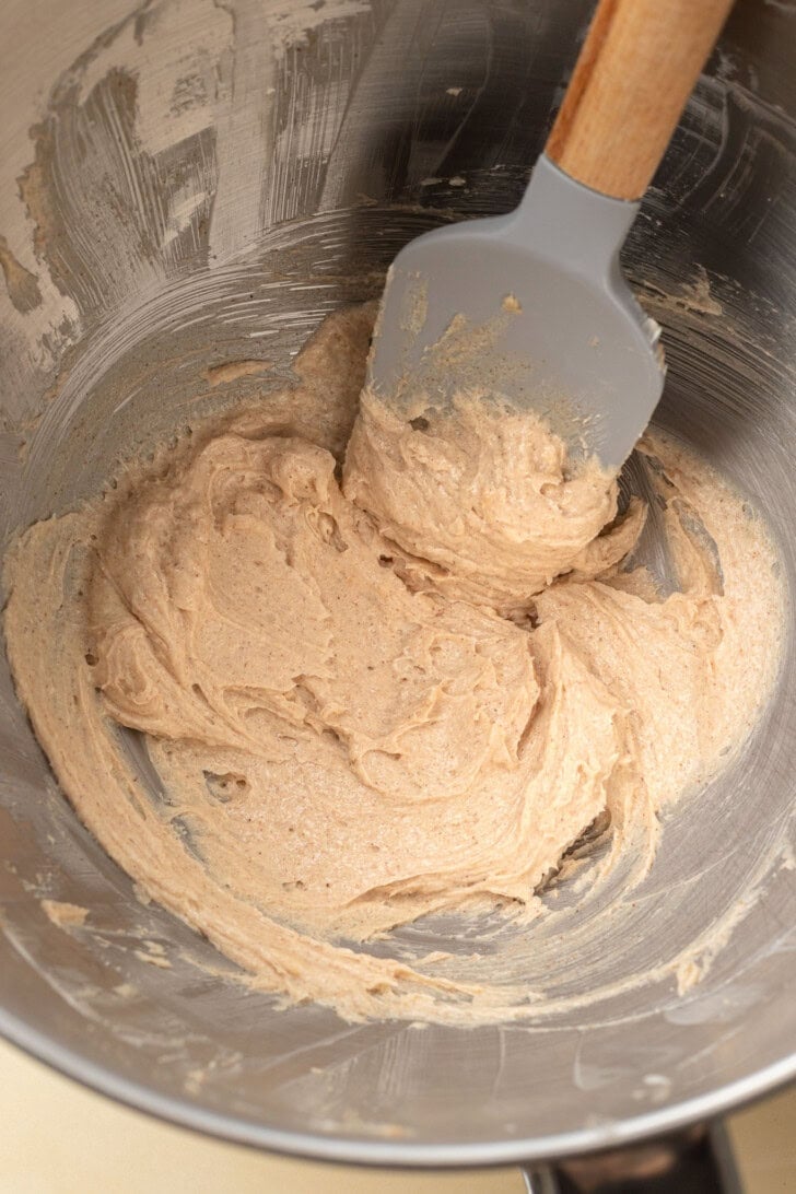 Thick butter being mixed in a metal bowl with a gray spatula.