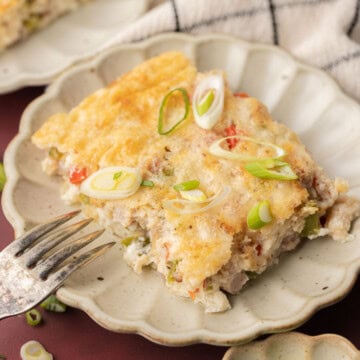 A slice of baked casserole topped with sliced green onions on a plate, with a fork and more onions nearby.